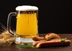 Kufel z piwem obok kiełbasek i kłosów zboża