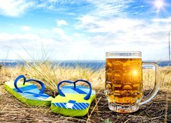 Kufel z piwem obok klapek na trawie