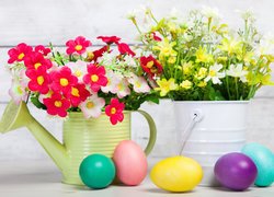 Kwiaty w konewce i wiaderku obok kolorowych jajek