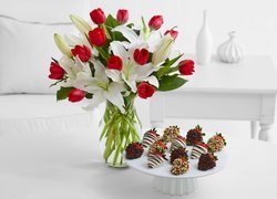 Kwiaty w wazonie obok patery z truskawkami w czekoladzie