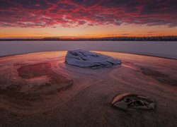 Las nad zamarzniętą rzeką pod kolorowym niebem