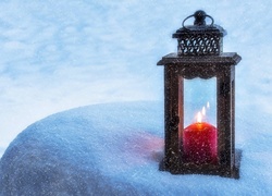 Latarenka z palącą się świecą stoi na zaśnieżonym kamieniu