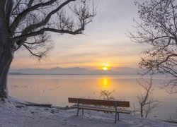 Ławka w śniegu z widokiem na zachód słońca nad jeziorem