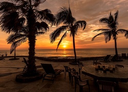 Leżaki i stolik z krzesłami pod palmami w blasku zachodzącego słońca