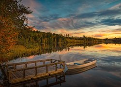 Łódka i pomost nad jeziorem o zachodzie słońca