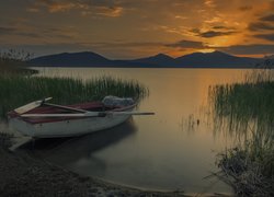 Łódka na brzegu jeziora na tle zachodzącego słońca