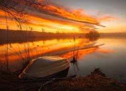 Łódka na brzegu jeziora w blasku zachodzącego słońca