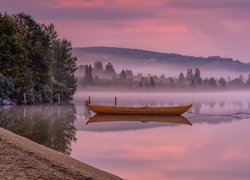 Łódka nad brzegiem zamglonego jeziora