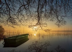 Łódka pod drzewami na jeziorze o zachodzie słońca