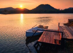 Łódka przy pomoście na jeziorze o zachodzie słońca