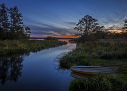 Łódka w zaroślach nad brzegiem rzeki o zachodzie słońca