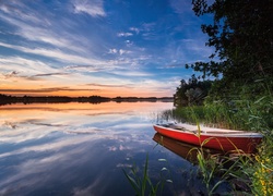 Łódka w zaroślach przy brzegu jeziora o zachodzie słońca