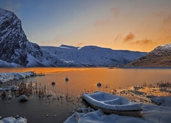 Łódka zasypana śniegiem nad jeziorem w blasku zachodzącego słońca