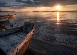 Łódki na brzegu jeziora w zachodzącym słońcu