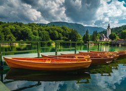 Łódki przy pomoście i kościół nad jeziorem Bohinj w Słowenii