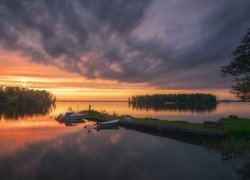 Łódki przy pomoście na jeziorze o zachodzie słońca