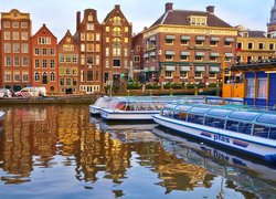 Łodzie wycieczkowe przy nabrzeżu kanału w Amsterdamie