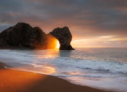 Łuk wapienny i plaża nad morzem na wybrzeżu Jurajskim w hrabstwie Dorset o zachodzie słońca