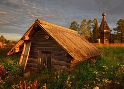 Mały drewniany domek na tle cerkwi