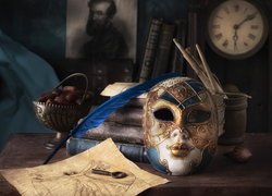 Maska karnawałowa obok starych książek i gęsiego pióra