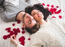 Mężczyzna i kobieta na łóżku obok płatków róż