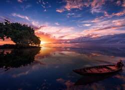 Mężczyzna na łódce na jeziorze o zachodzie słońca