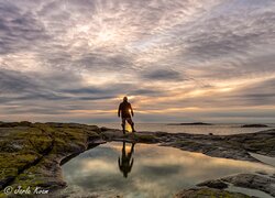 Mężczyzna na skalistym brzegu nad morzem o zachodzie słońca