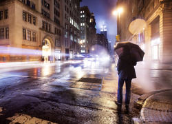 Mężczyzna po parasolem na oświetlonej ulicy nocą