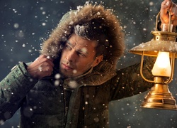 Mężczyzna podczas śnieżycy oświetla sobie drogę lampą
