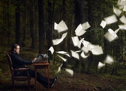 Mężczyzna przy maszynie do pisania i fruwające kartki w lesie