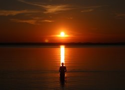 Mężczyzna w jeziorze wpatrzony w zachodzące słońce