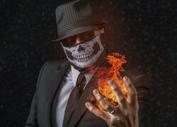 Mężczyzna w kapeluszu i masce z płomieniem w dłoni