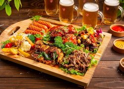 Mięso z warzywami na desce obok sosów i kufli piwa