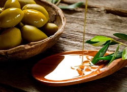 Miska z oliwkami postawiona na desce obok łyżki z olejem