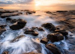 Morskie fale opłukują kamienie w blasku zachodzącego słońca