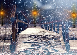 Most nad zamarzniętą rzeką w parku oświetlonym latarniami w prószącym śniegu