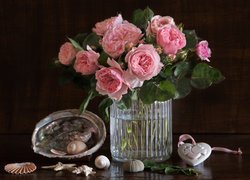 Muszelki obok różowych róż w szklanym wazonie