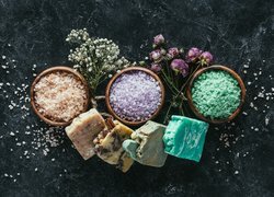 Mydła i kolorowa sól w miseczkach obok suchych kwiatów