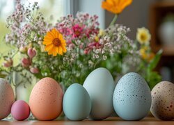 Nakrapiane pisanki obok bukietu kwiatów w wazonie