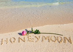 Napis honeymoon na piasku i róża