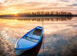 Niebieska łódka na brzegu jeziora w słońcu