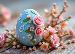 Niebieska pisanka ozdobiona różami na deskach wśród kwitnących gałązek i róż