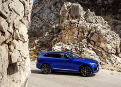 Niebieski Jaguar F-Pace S na drodze pośród skał