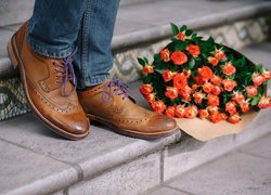 Nogi mężczyzny w brązowych butach obok bukietu róż