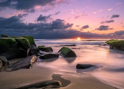 Omszałe głazy na morskiej plaży w blasku zachodzącego słońca