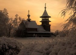 Ośnieżona cerkiew i drzewa na tle pomarańczowego nieba