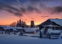 Ośnieżone domy i cerkiew o zachodzie słońca