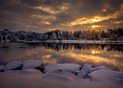 Ośnieżone drzewa i kamienie nad rzeką wieczorem