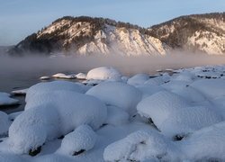 Ośnieżone kamienie i opadająca mgła nad jeziorem