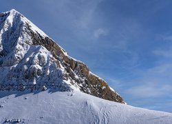 Ośnieżony szczyt i zbocza skalistej góry na tle nieba